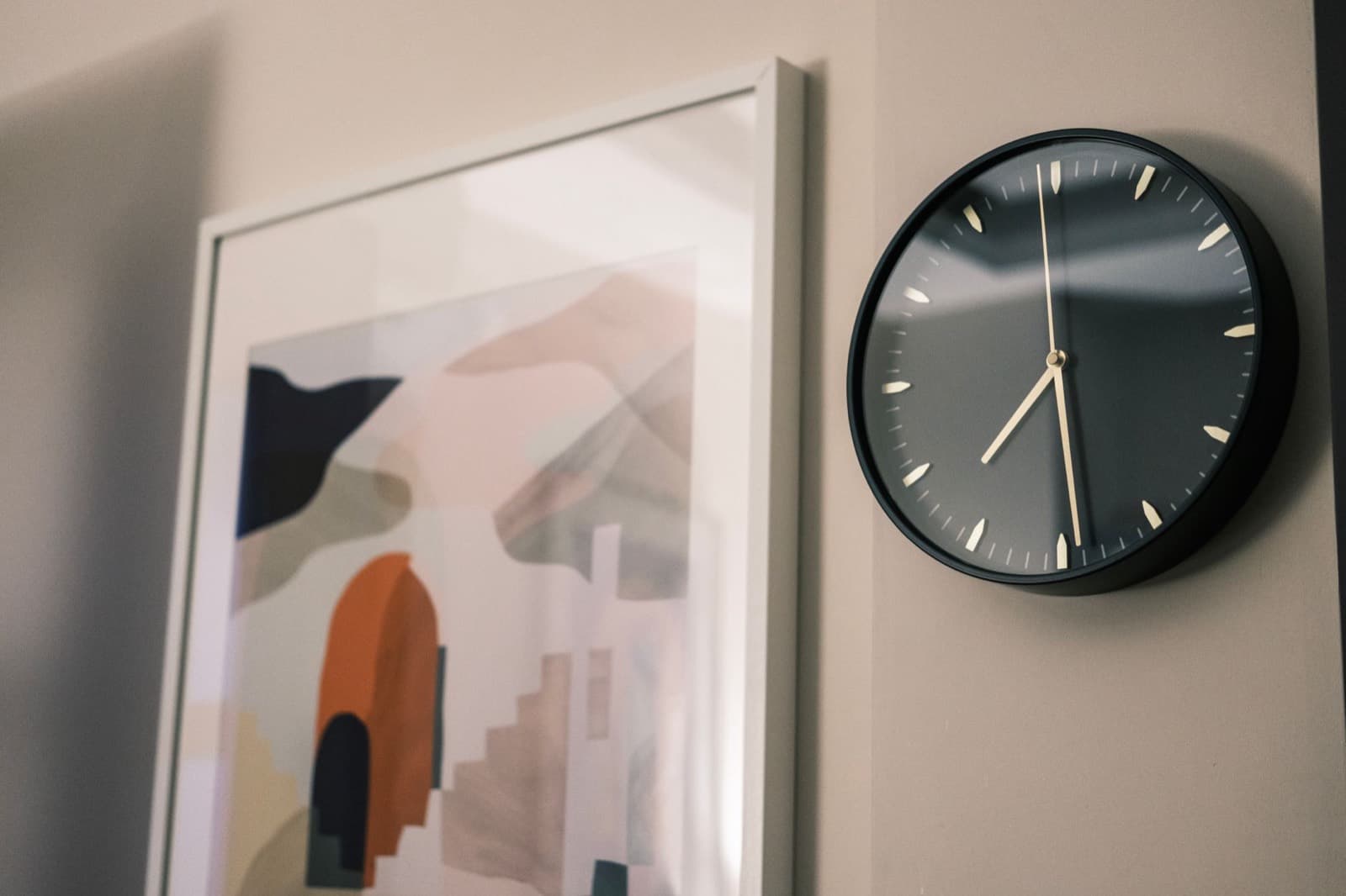 A plain black wall clock beside an abstract print